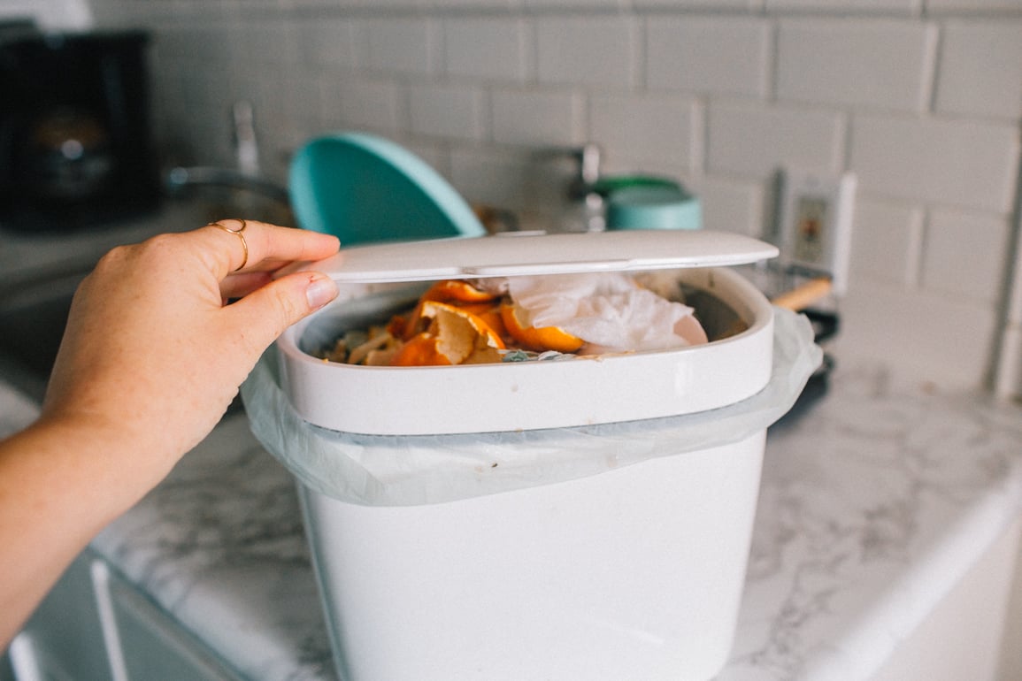woman puts food waste into white compost bin
